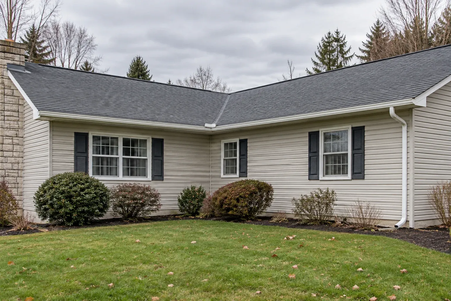 Single-story L-shaped house with a shingle roof valley above an inside gutter corner and a downspout along one wall.