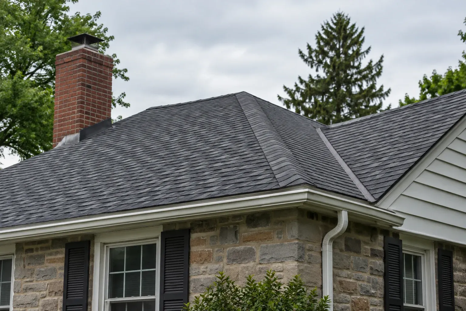 Ground-level view of an asphalt-shingle roof with a chimney and gutters.