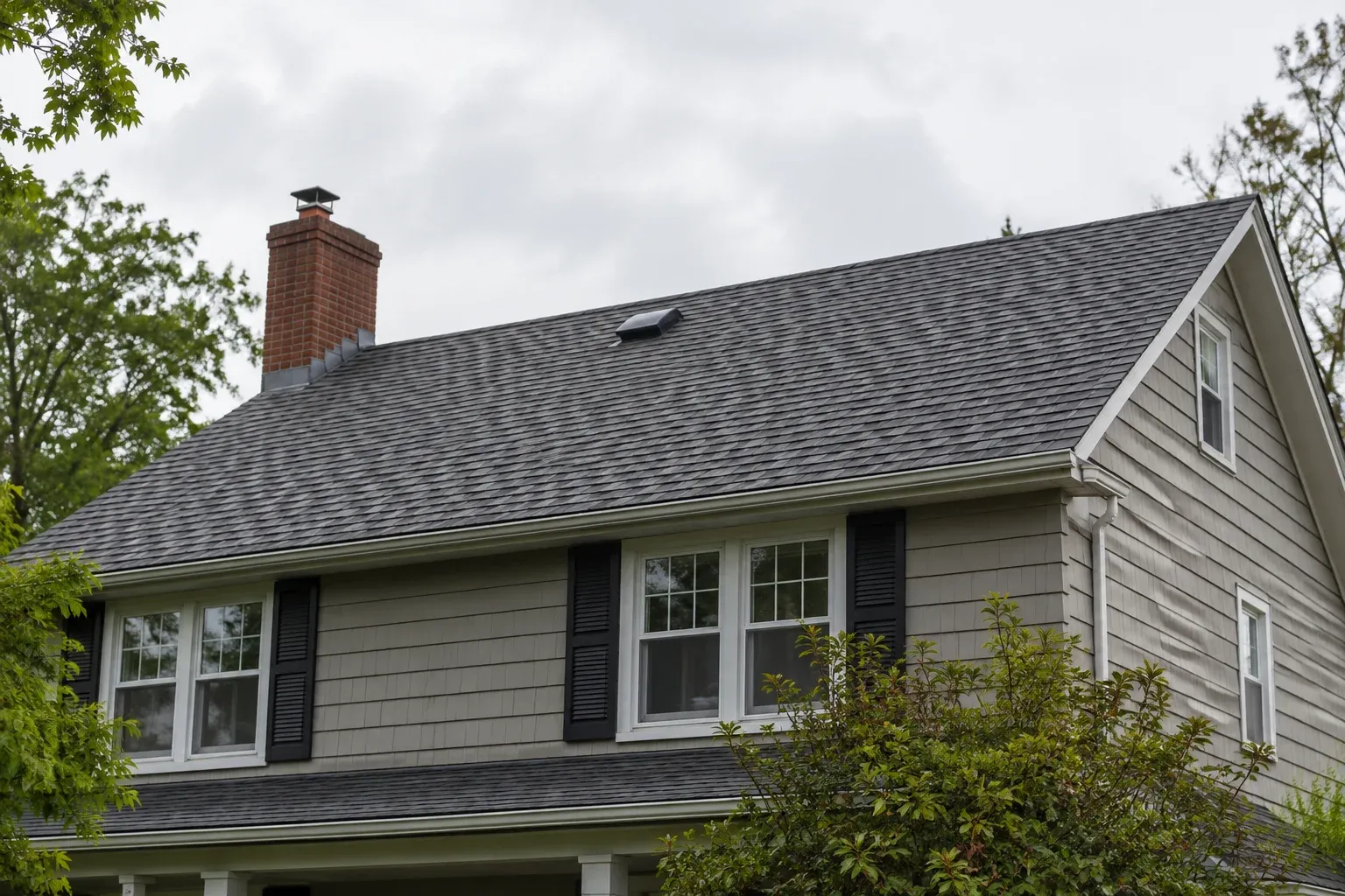 Ground-level view of a shingle roof and upper-story exterior under overcast skies.